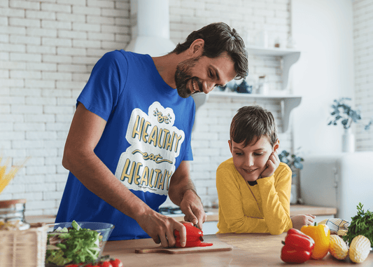 A man and boy cutting vegetables in a kitchen, showcasing the Be Healthy Eat Healthy Unisex T-Shirt. Made from soft 100% ring-spun cotton, featuring twill tape shoulders for durability and a clean crew neckline.