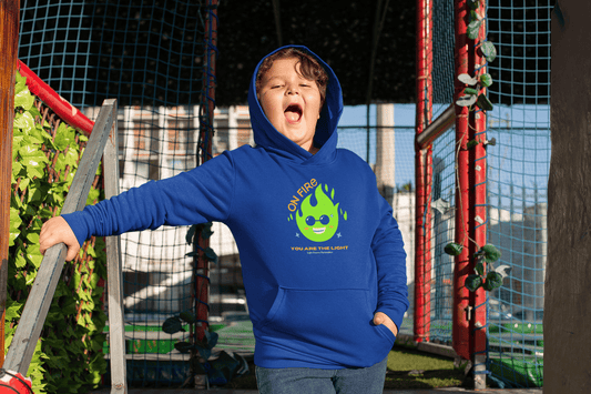 A boy in a blue hoodie with a cartoon fire design, showcasing the On Fire You are the Light Youth Hooded Sweatshirt. Kangaroo pocket, soft fleece, 50% cotton 50% polyester blend.