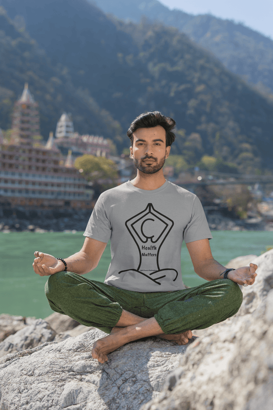 A man in a soft-style unisex t-shirt sits on a rock by a body of water. Made of 100% cotton, this tee offers comfort and durability with twill tape shoulders and ribbed collar.