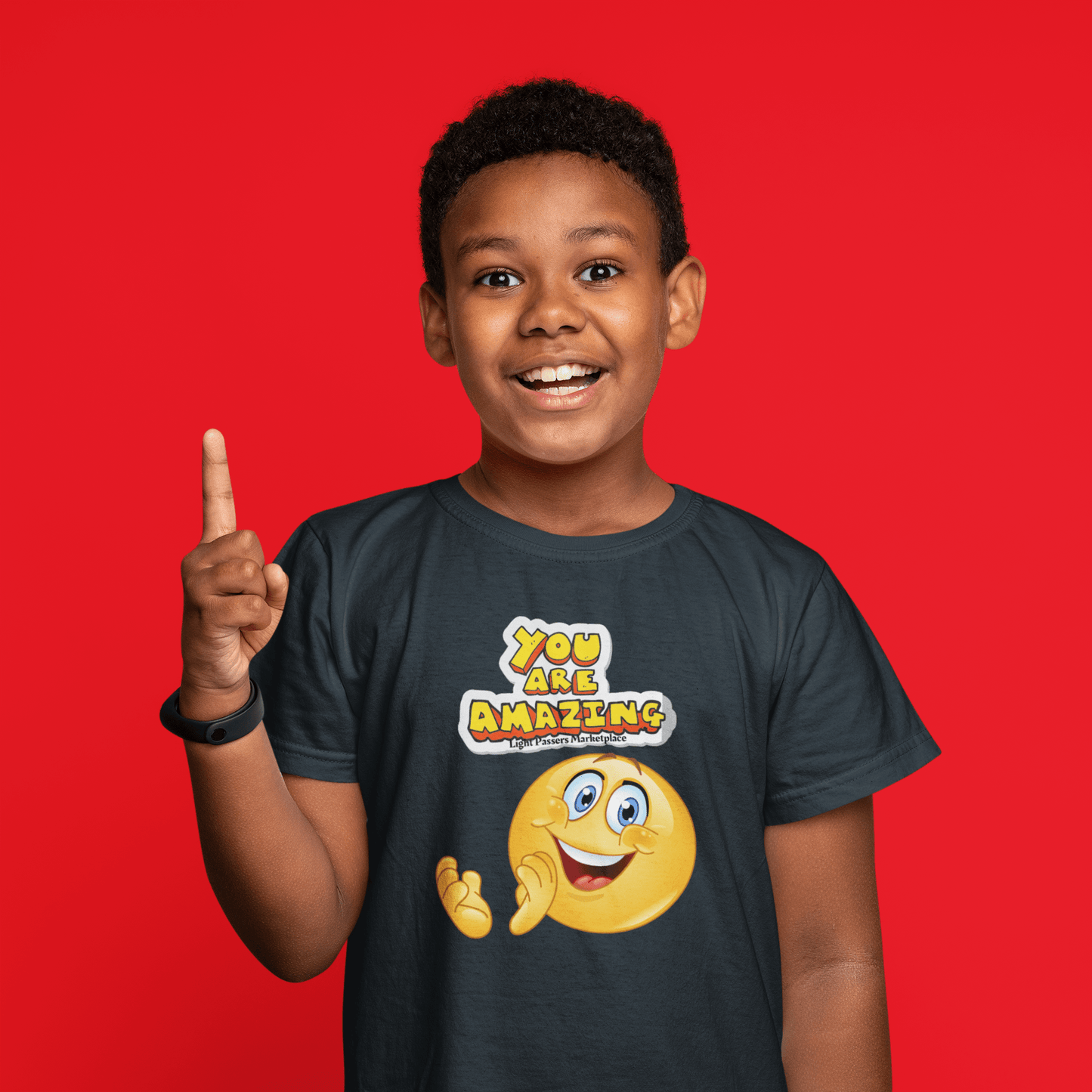 A boy in a You are Amazing Clap youth t-shirt, pointing up, with a smiley face sticker and text details. Combed ring-spun cotton, soft-washed, garment-dyed, classic fit for comfort and agility.