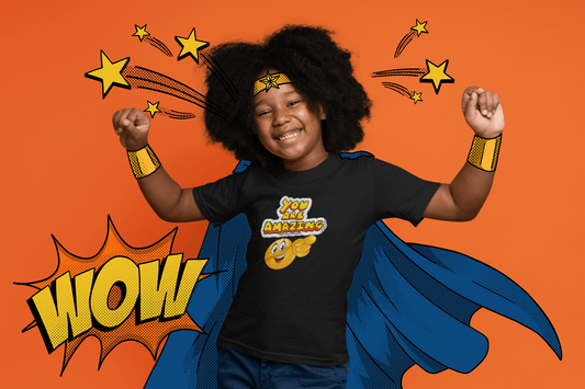 A child in a superhero garment smiles, a yellow star on an orange background, with a cartoon smiley face pointing. Kids heavy cotton tee, 100% cotton, twill tape shoulders, curl-resistant collar, no side seams.