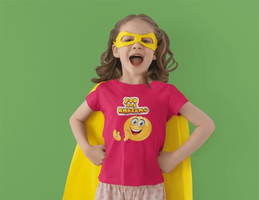 A toddler wearing a garment and mask, smiling. A close-up of a child in a yellow mask. Product: You are Amazing Toddler T-shirt, soft, durable, with a high-quality print, 100% combed cotton.