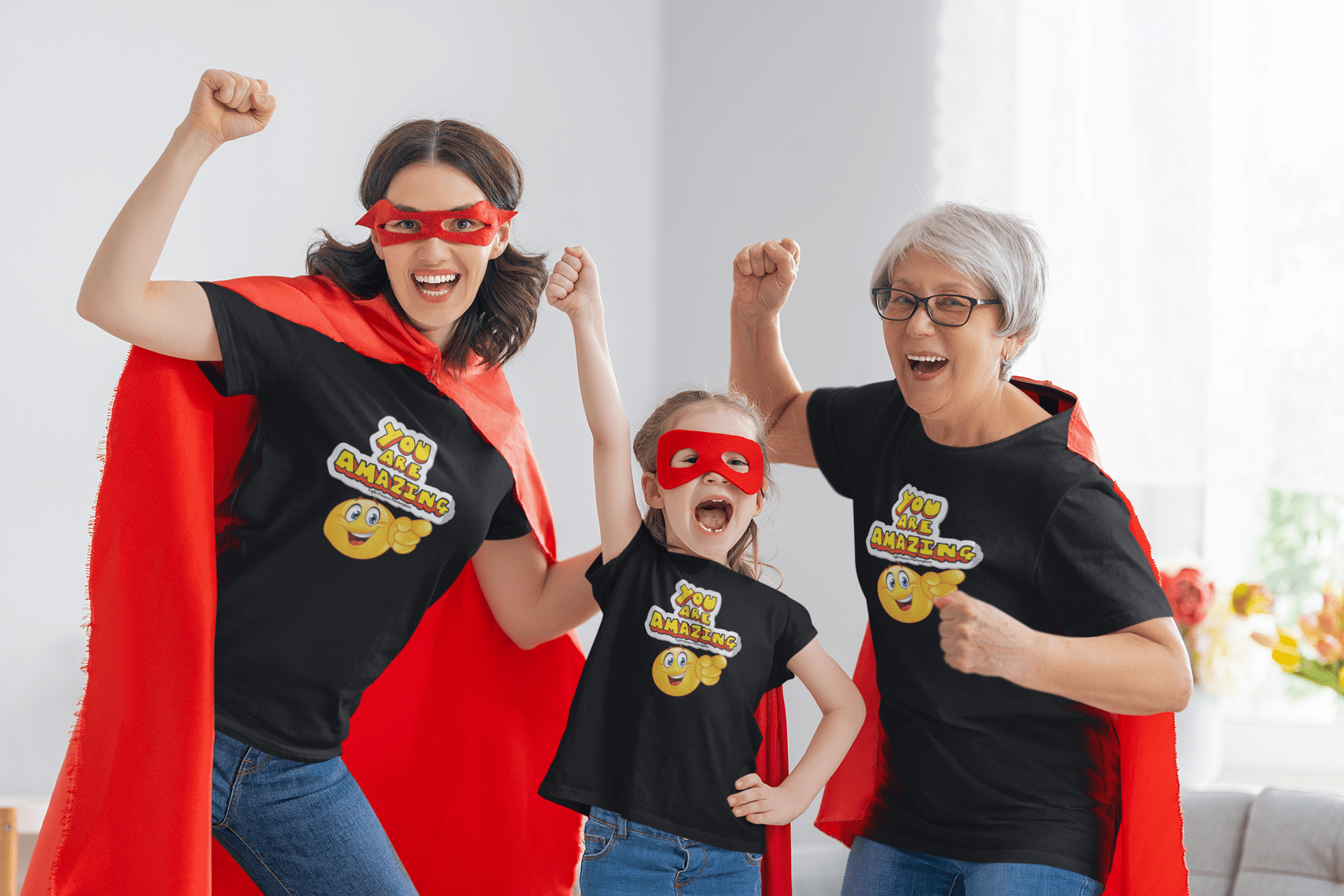 A group of women and a girl in superhero clothing, a woman in a red cape and mask, a girl in a mask and black shirt, and a child in a red mask. Alt text: You are Amazing emoji pointing Toddler Tee, featuring superhero-themed clothing for toddlers with soft 100% combed cotton and durable print.