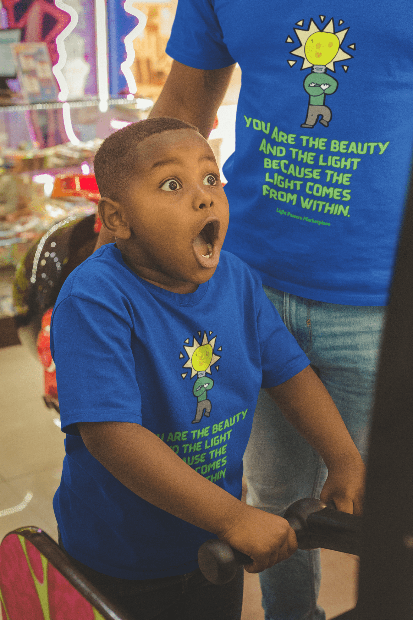 A boy in a blue shirt gazes at a cartoon light bulb, embodying creativity and wonder on the Beauty and the Light Youth T-shirt. Soft cotton, high-quality print, tear-away label, and a regular fit ensure comfort and style.