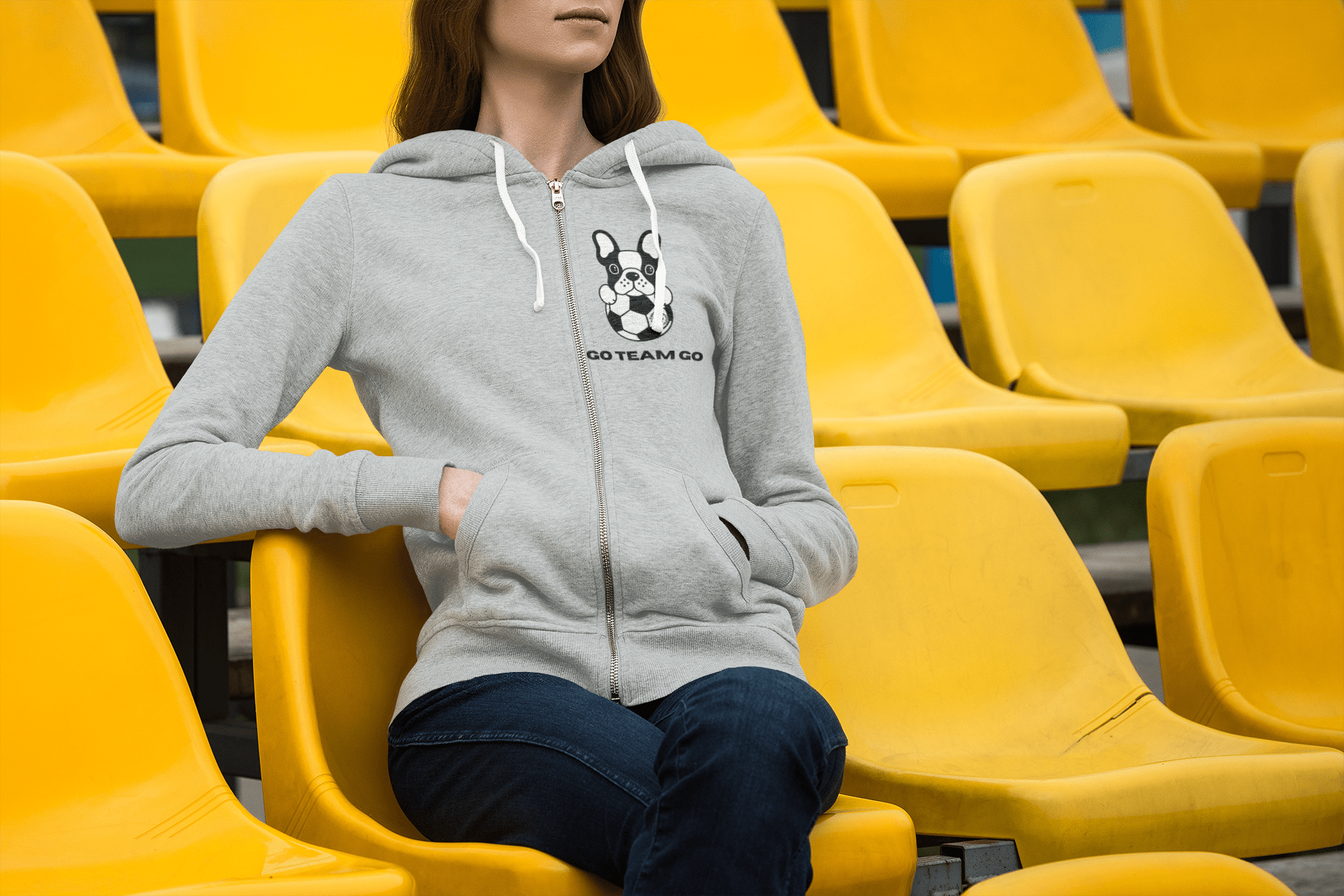 A woman in a yellow stadium seat, showcasing a Soccer Dog Unisex Full Zip Hooded Sweatshirt. Medium-heavy fabric, classic fit, and soft fleece for ultimate comfort.