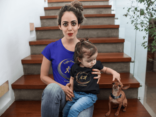 Toddler's Tee 'Do Good Deeds' Light Passers Relay Design, shown worn by a smiling toddler sitting with a woman on stairs, emphasizing comfort and cheerful design.