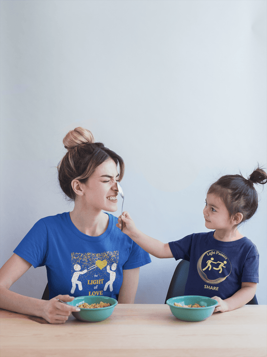 Toddler wearing Love Others Light Passers Relay T-shirt, eating cereal with a woman, highlighting the tee's softness and comfortable fit for sensitive skin.