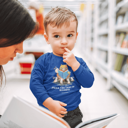 Toddler Long Sleeve Pass the Light of Reading: A toddler in a library wearing a blue long-sleeve tee, showcasing durable cotton fabric and tear-away label.