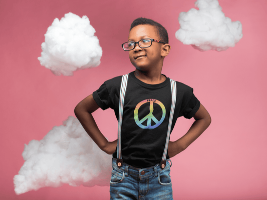 A boy in a black tee with suspenders, standing by a rainbow peace sign, cotton clouds in hand. Kids heavy cotton tee, 100% cotton, durable twill tape shoulders, ribbed collar, seamless sides.