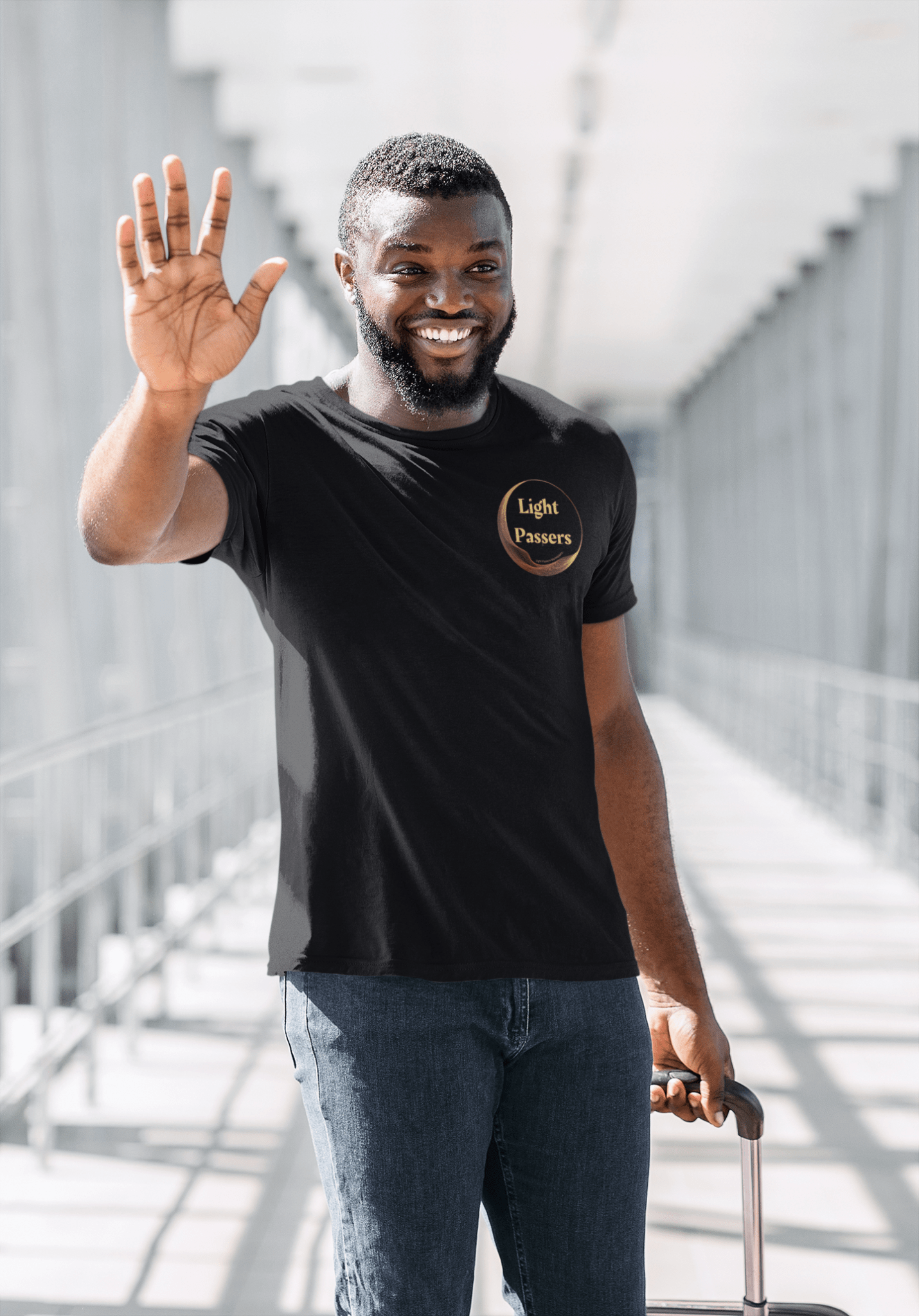 A man in a hallway wearing a black shirt and jeans, smiling at the camera. Close-ups of hands holding a black tube and metal rod. Product: Small Light Passers Logo Unisex T-shirt.