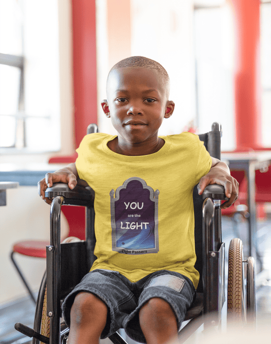 A toddler in a wheelchair wearing the Light Mirror Toddler T-shirt, showcasing a durable print on soft cotton fabric. Classic fit, tear-away label, ideal for sensitive skin.