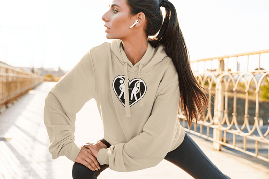A woman stretches her leg in a heart logo sweatshirt. Unisex heavy blend hooded sweatshirt with kangaroo pocket, drawstring hood, and cozy cotton-polyester fabric.