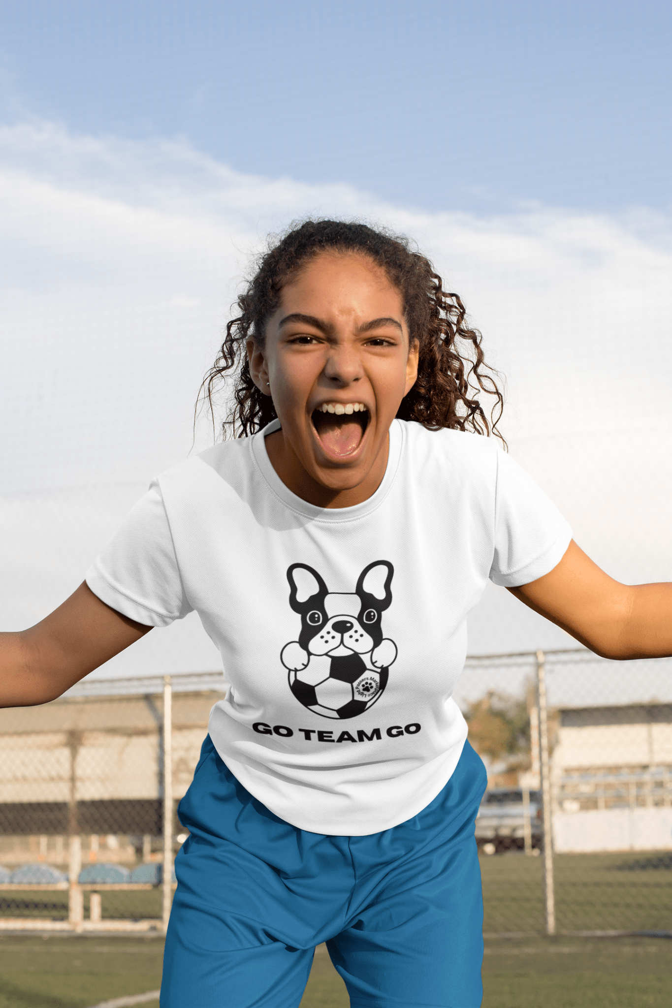 A black and white dog with a football ball, a girl with her mouth open, and a person in blue pants featured on the Soccer Dog Unisex T-Shirt. Made from soft 100% cotton with twill tape shoulders and ribbed collar.