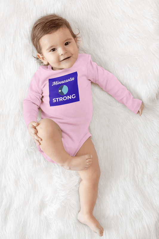 Infant in “Minnesota Strong” onesie on a soft surface, embodying resilience and comfort, ideal for Light Passers Marketplace’s community-focused, inspirational product range.
