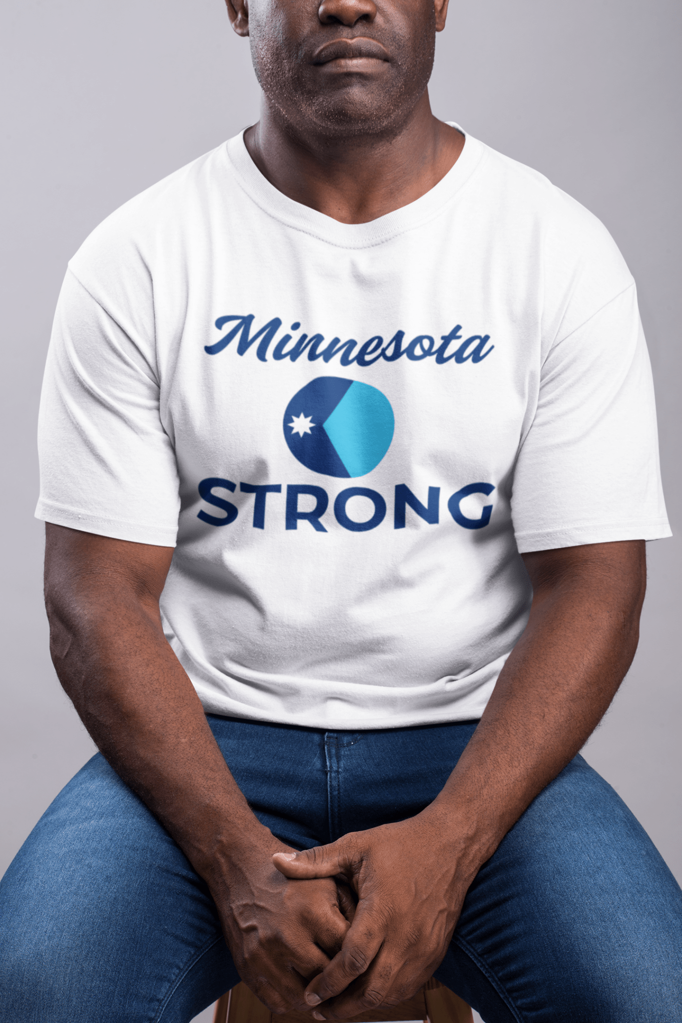 Love and Peace The Light Adult Unisex Minnesota Strong T-Shirt, featuring the Minnesota STRONG message with a circular logo, worn by a seated man.