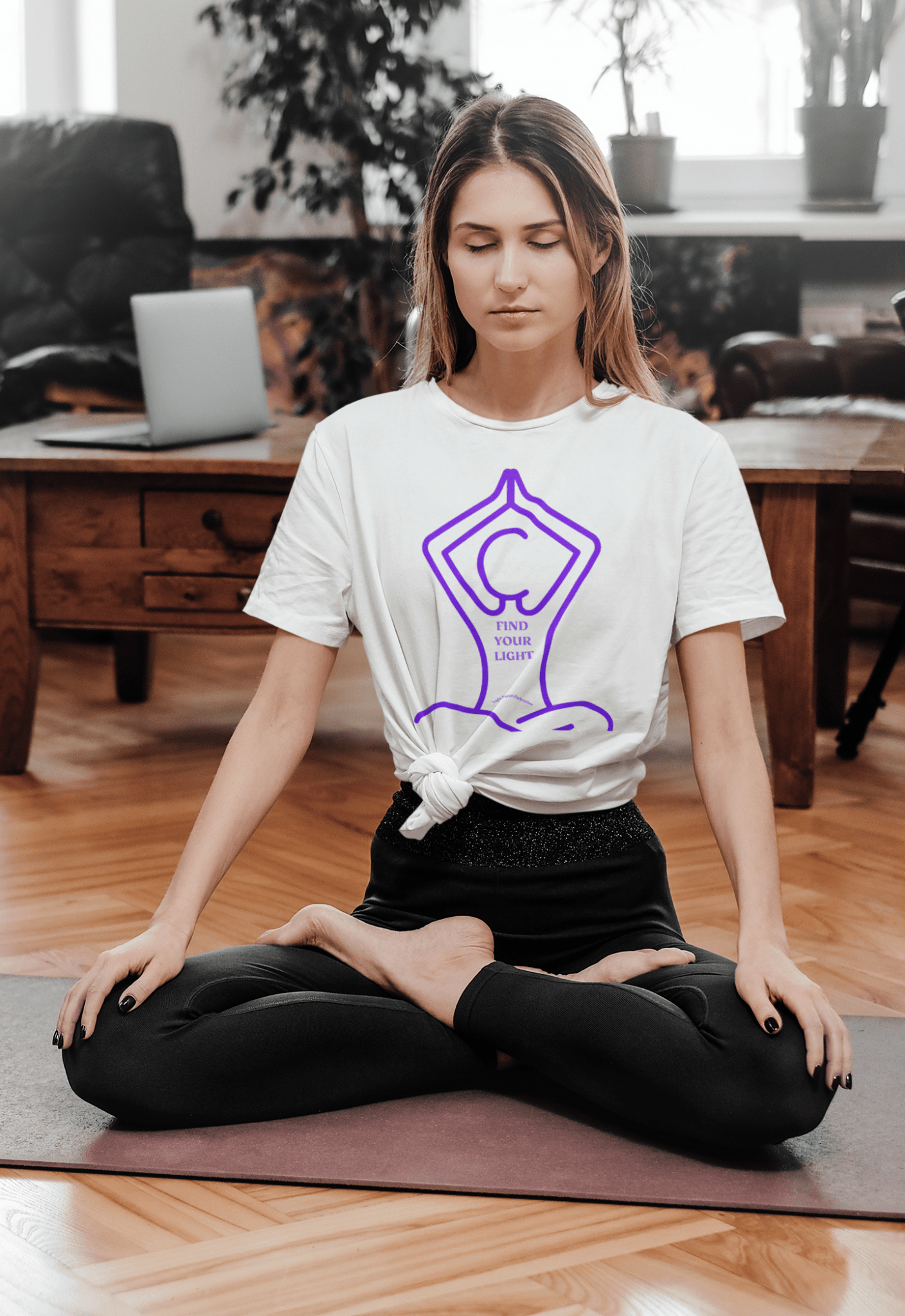 A woman in a room, sitting cross-legged, wearing the Yoga Find Your Light Unisex T-shirt. Close-up of the shirt's smooth fabric, no side seams for comfort. Classic fit, 100% cotton.