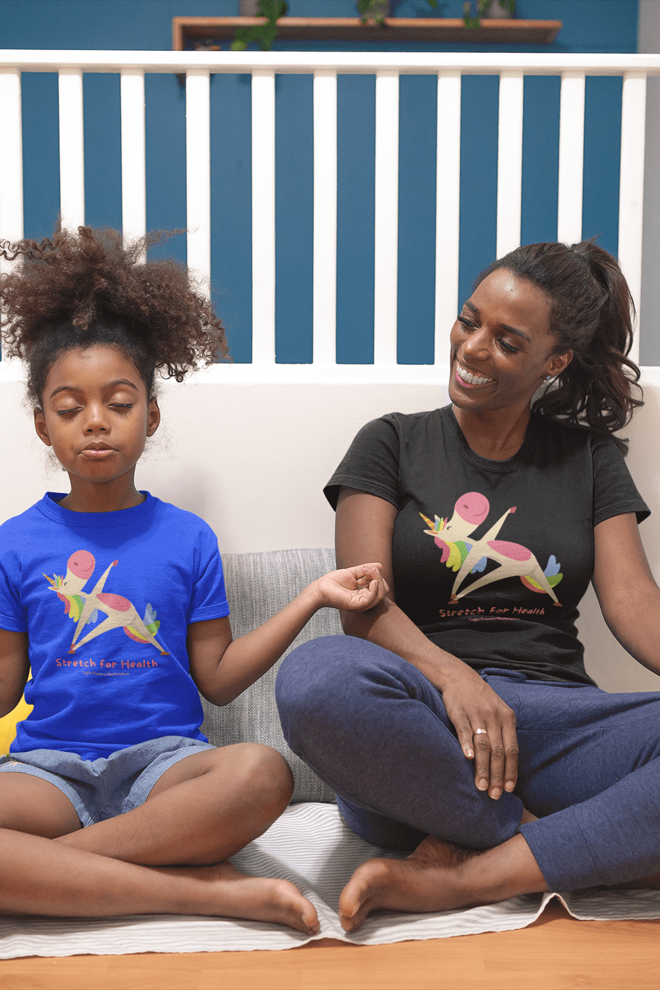 A woman and a girl sitting on a couch, both wearing a Unicorn Stretch Yoga Youth T-shirt. The tee is 100% cotton, featuring twill tape shoulders and ribbed collar for durability and comfort.